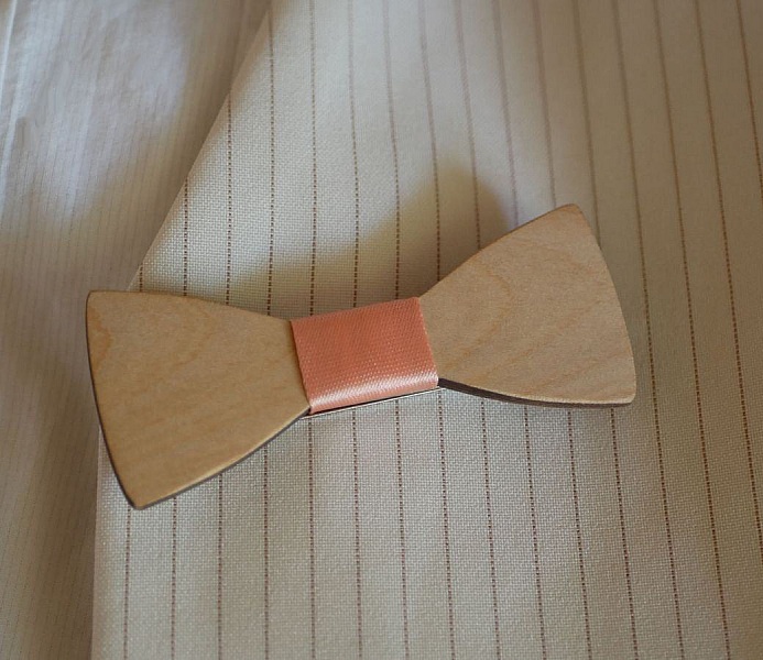 Nœud papillon en bois avec ruban rose sur chemise rayée.