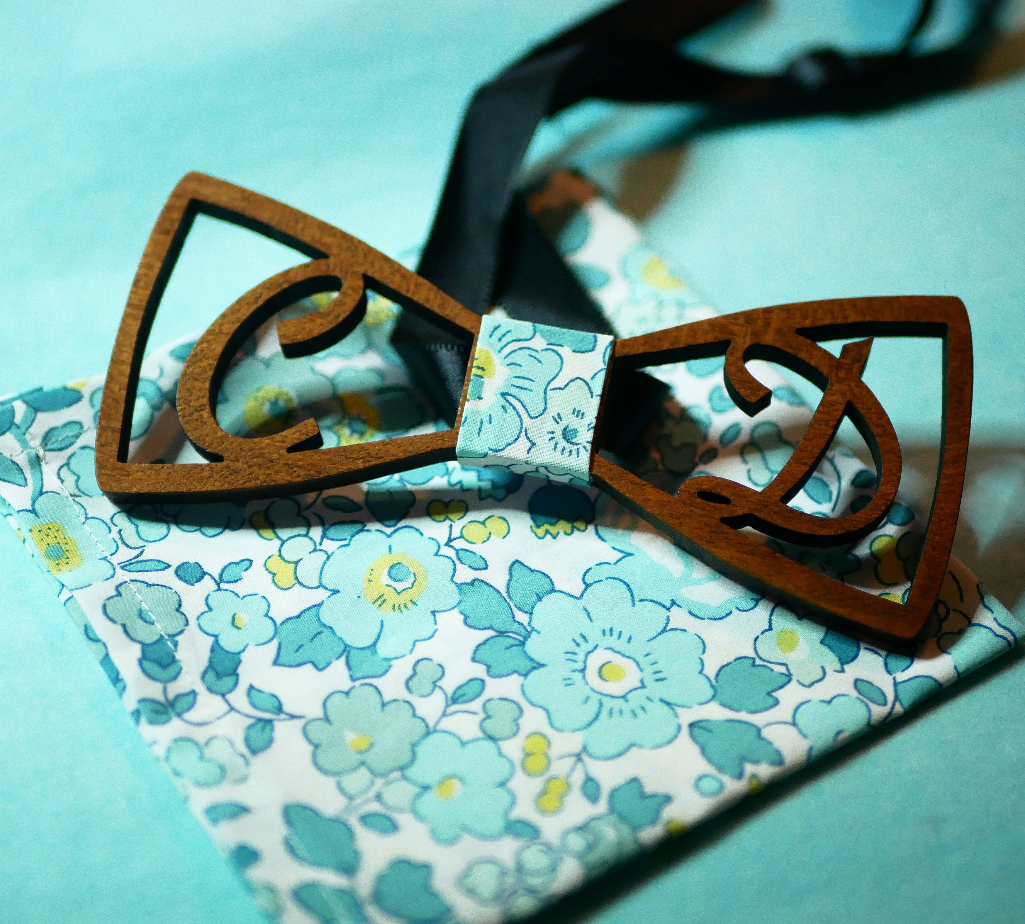 Nœud papillon en bois ajouré sur tissu floral bleu.
